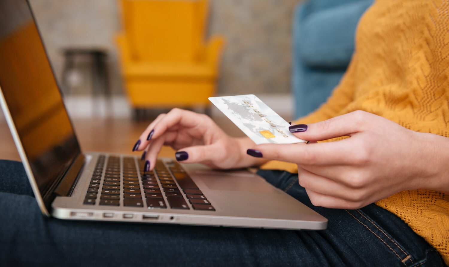 Close up of a woman buying on line with bank card and typing on laptop while sitting in the living room at home